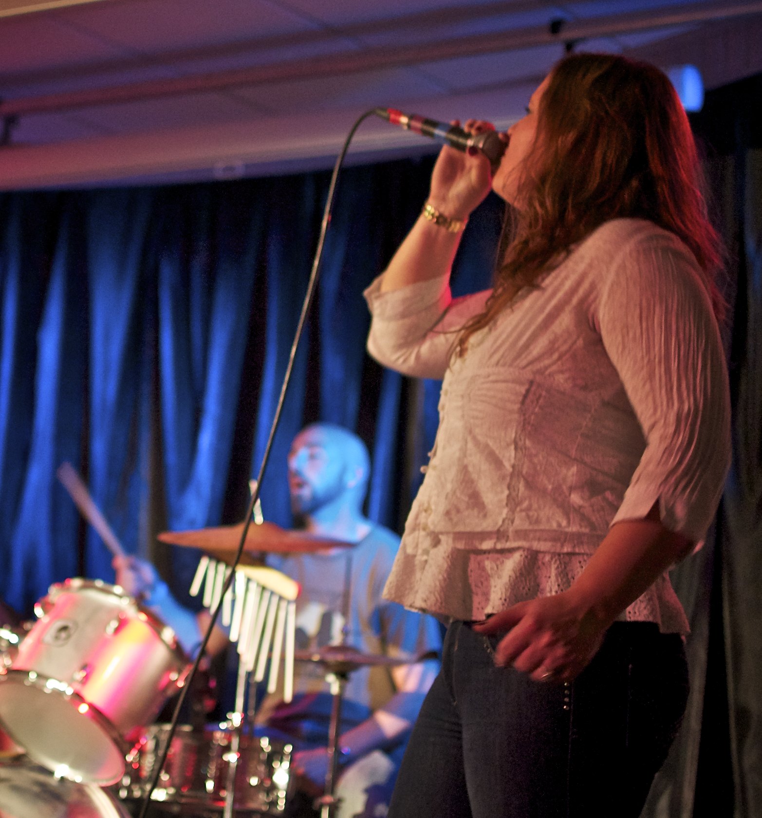 a woman singing into a microphone while standing in front of the drums