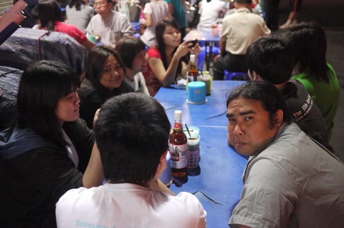 a crowd of people gathered together at a table with a beer bottle