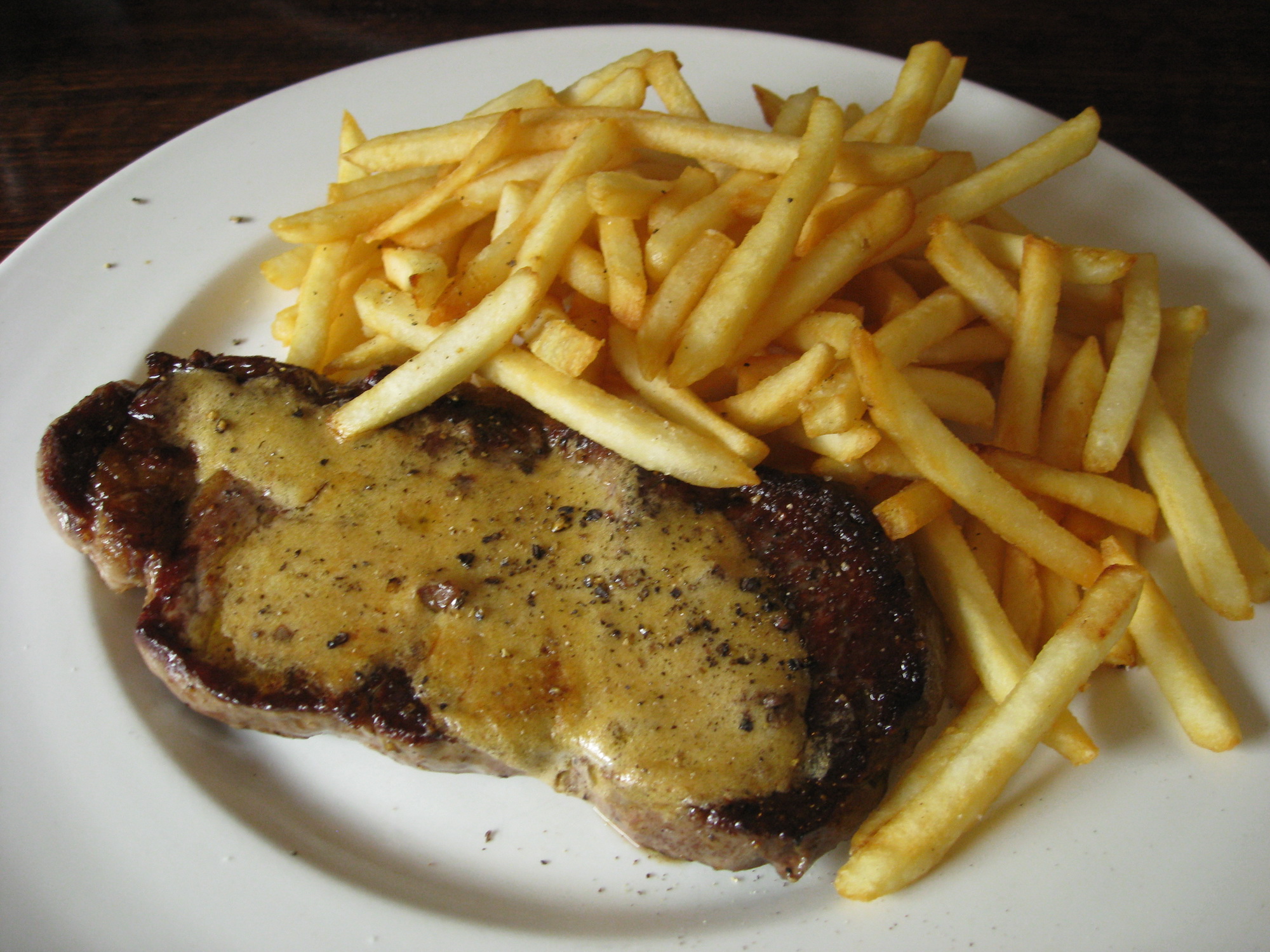 a steak with sauce and french fries are served on a plate