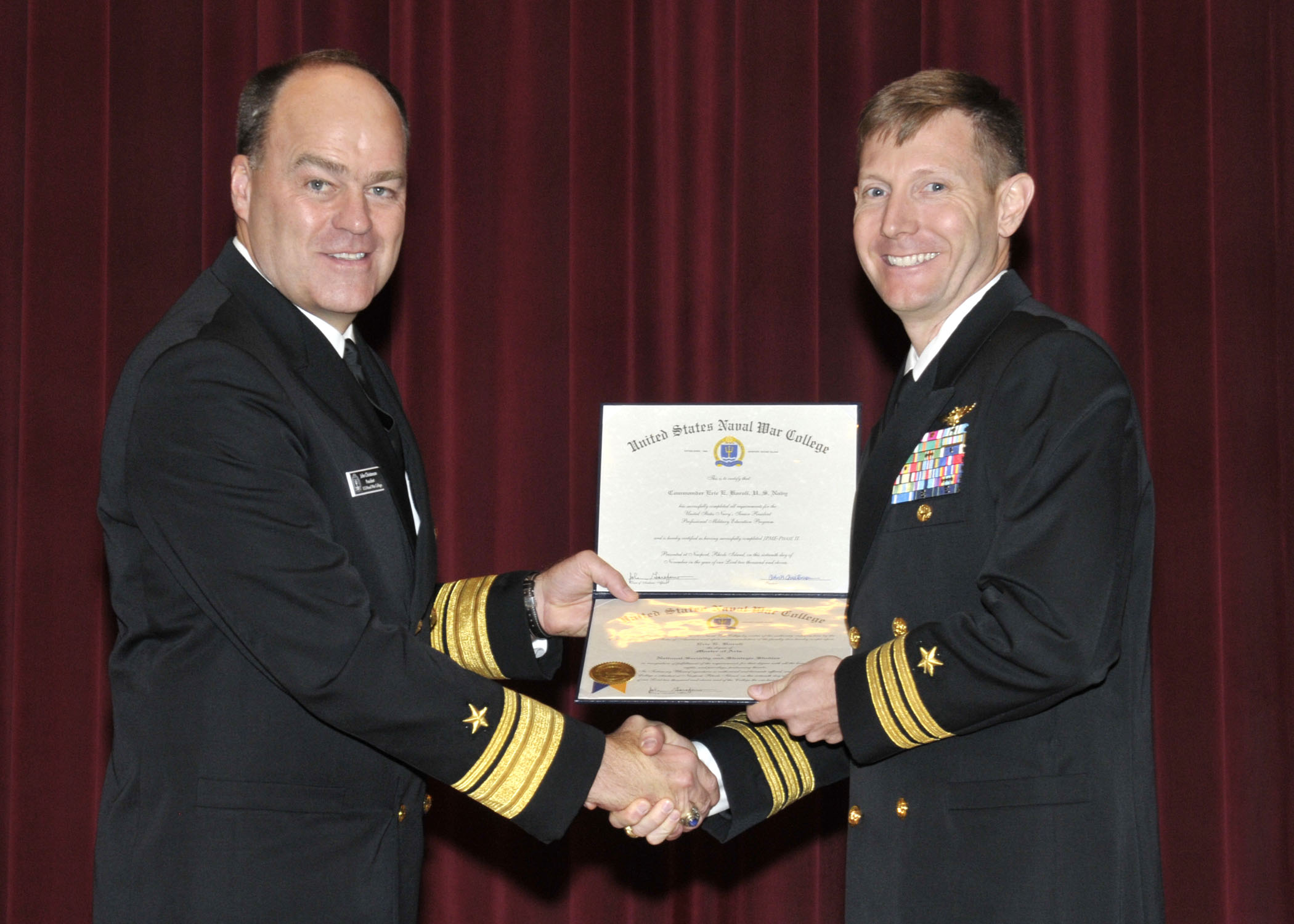 two sailors shaking hands while holding an award