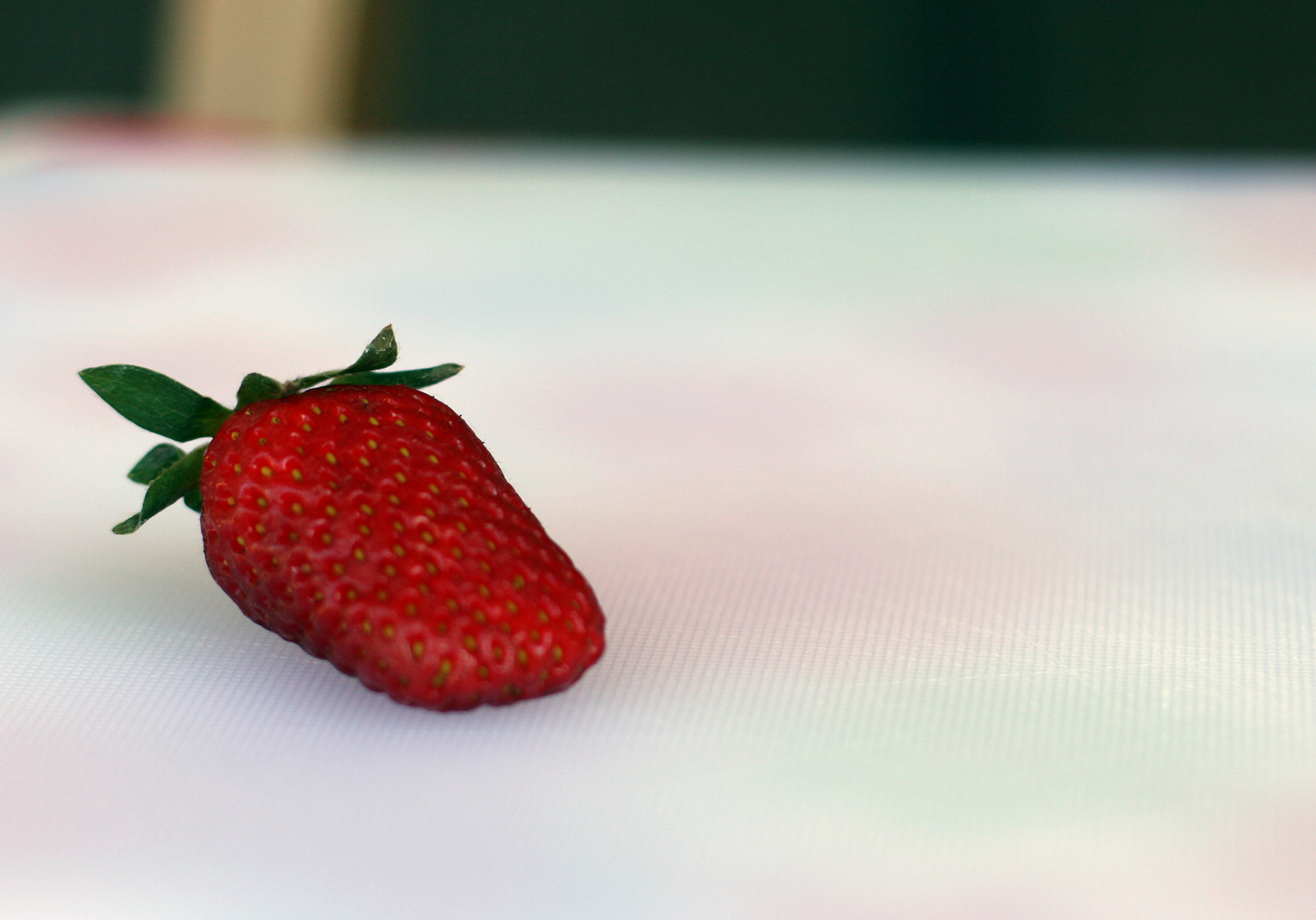 a strawberries sits on a table with its end facing the camera