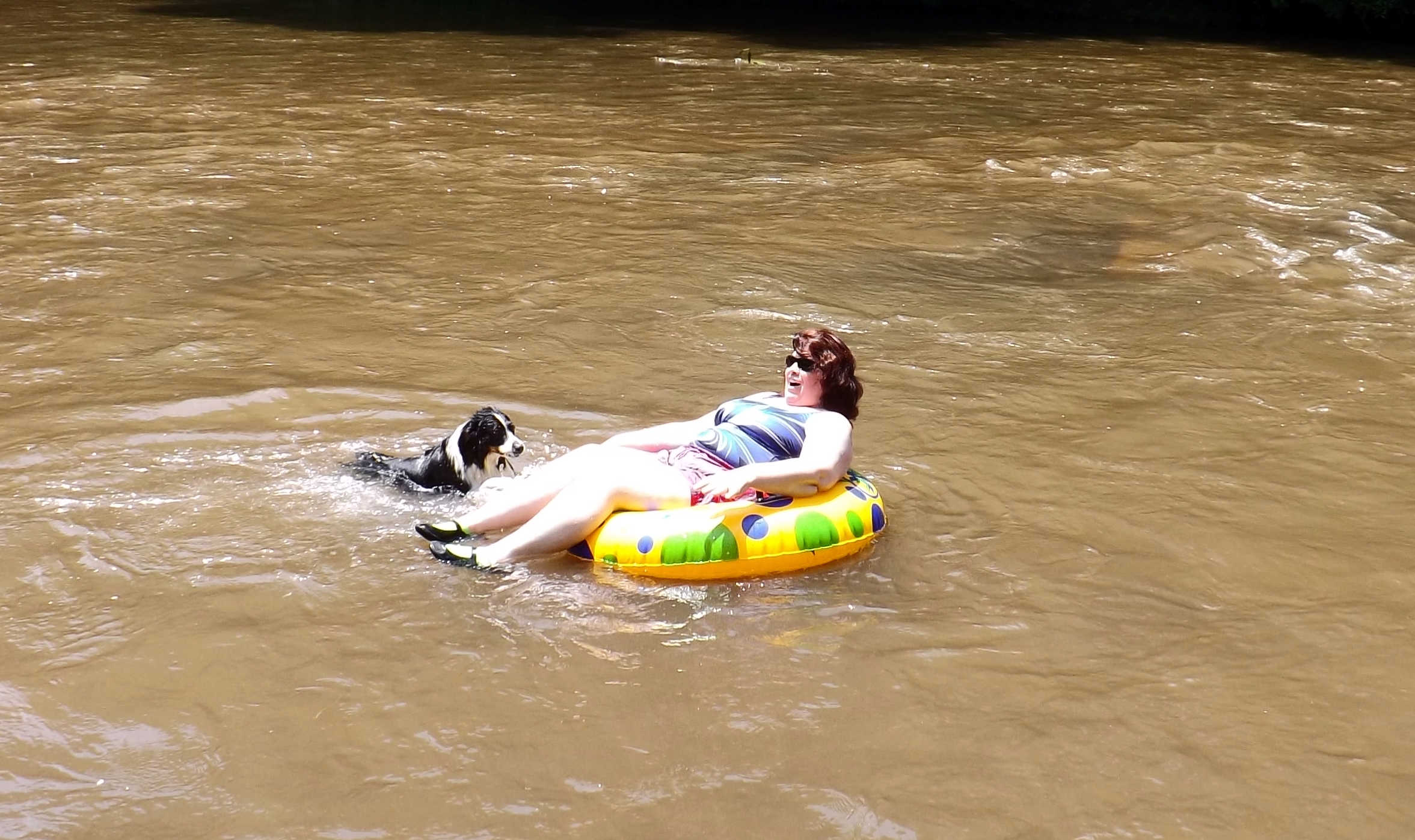 the girl is having fun floating in the brown water with her dog