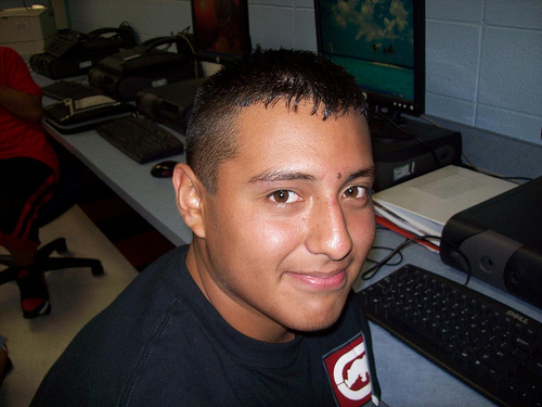 the young man smiles as he poses with his computer in the background
