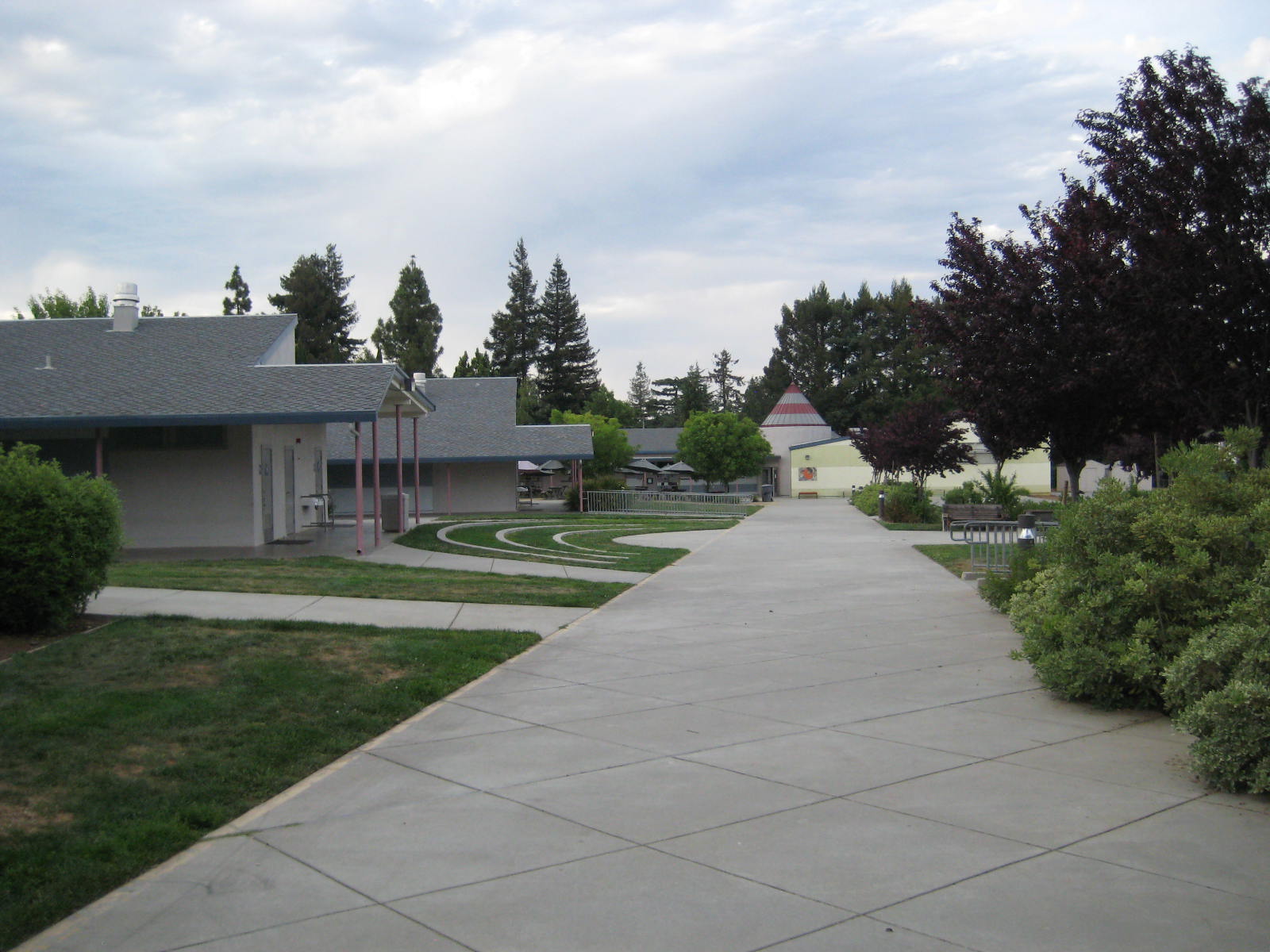 a cement walkway leading to a building with some trees and bushes