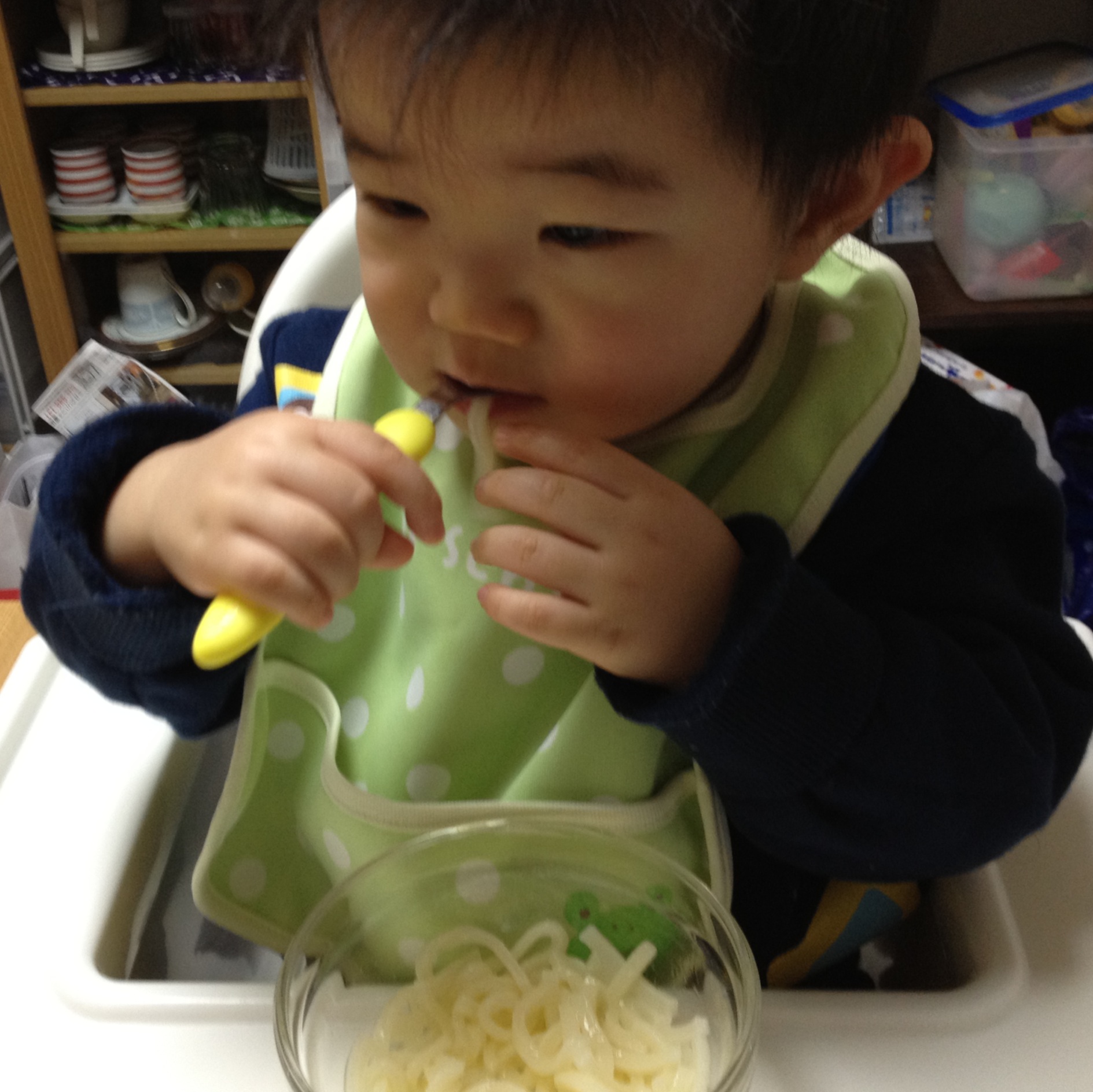 a child in a green bib with a yellow pen in their mouth and pasta in a bowl