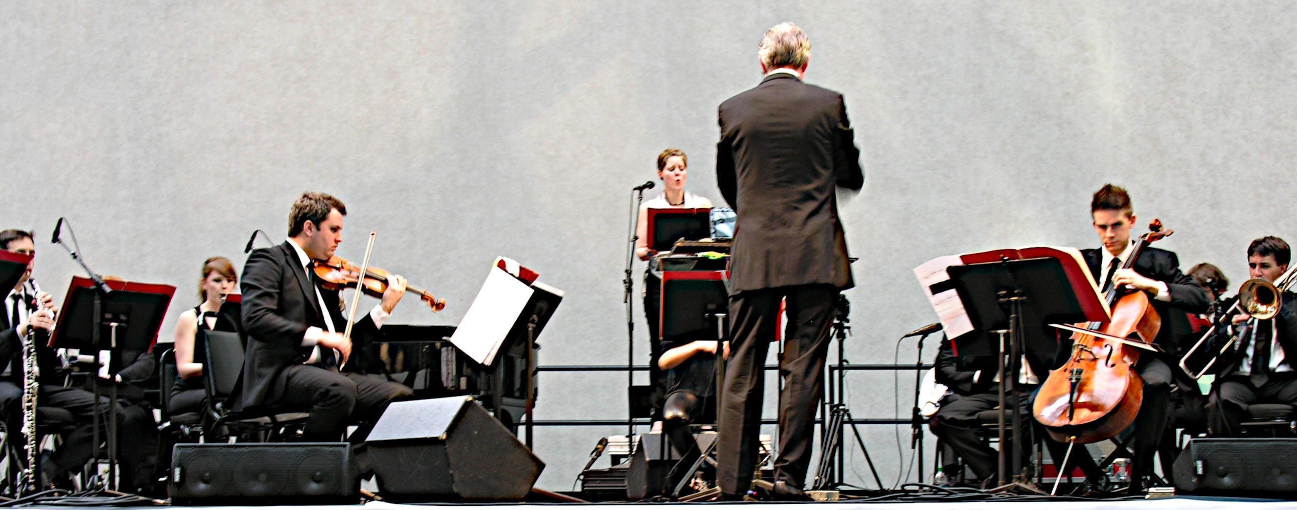 a man stands in front of a orchestra and a conductor