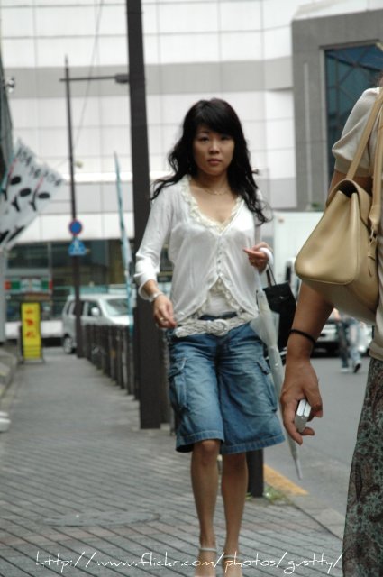 a woman wearing blue jean shorts and heels walks down the street