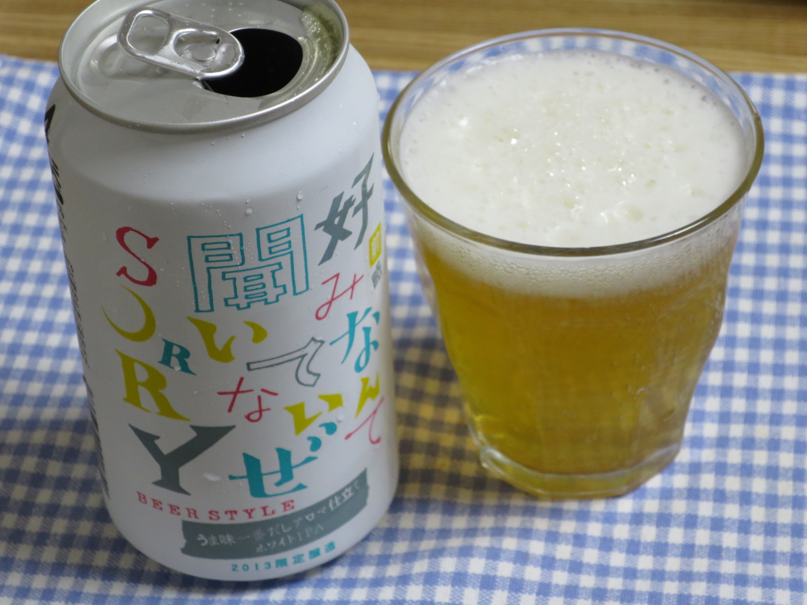 an empty can and a glass of beer sit on a checkered cloth