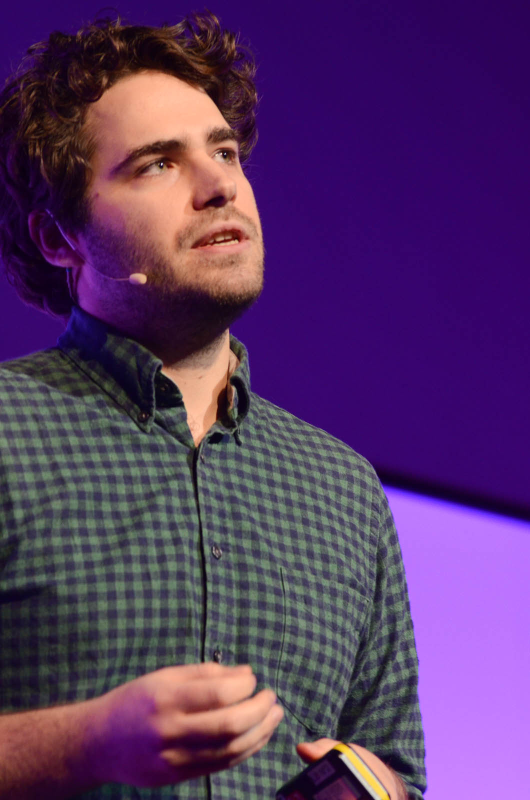 a man in a black and green checkered shirt is talking into a microphone