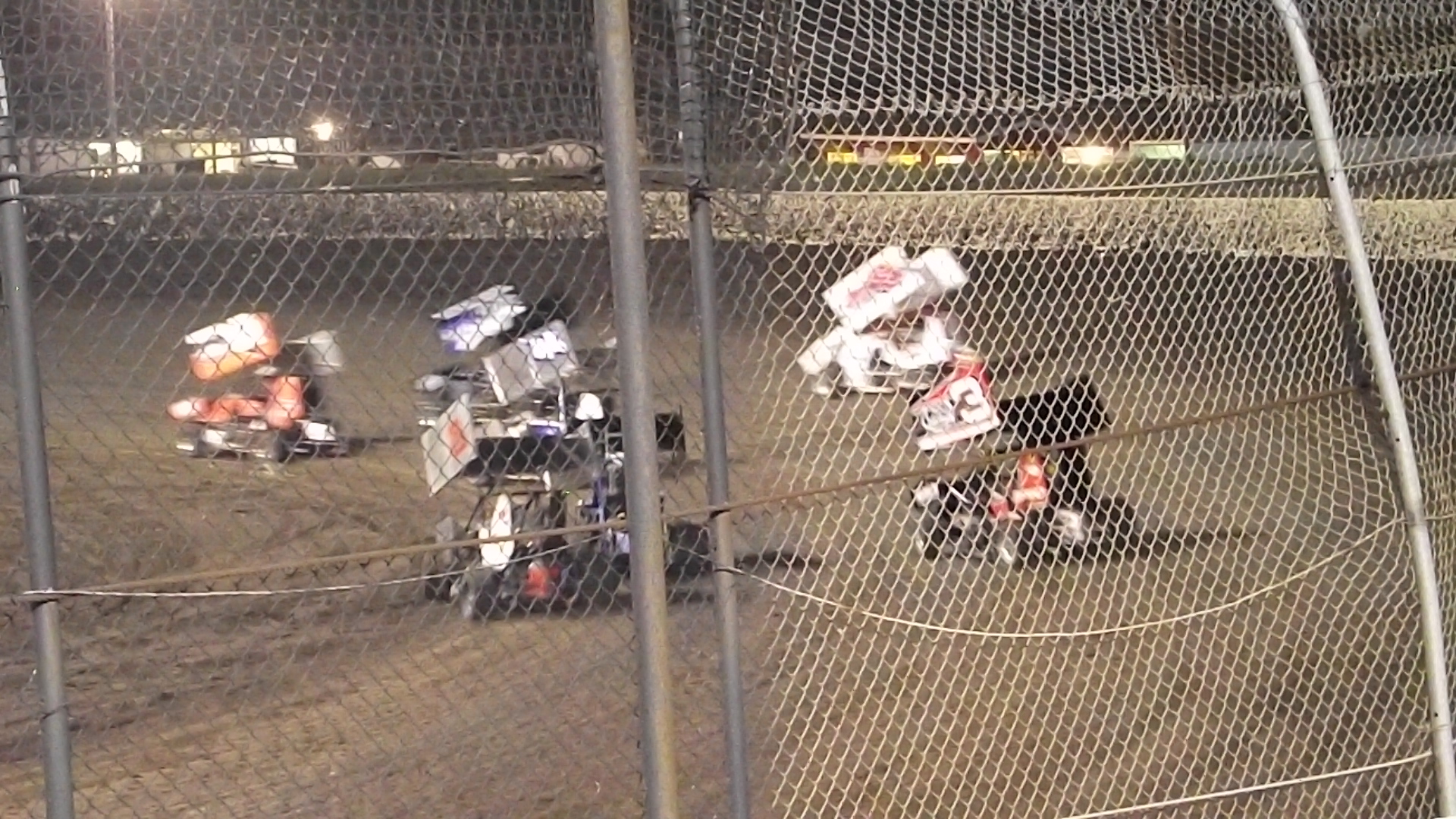 a group of people playing on a dirt track in a fenced off area