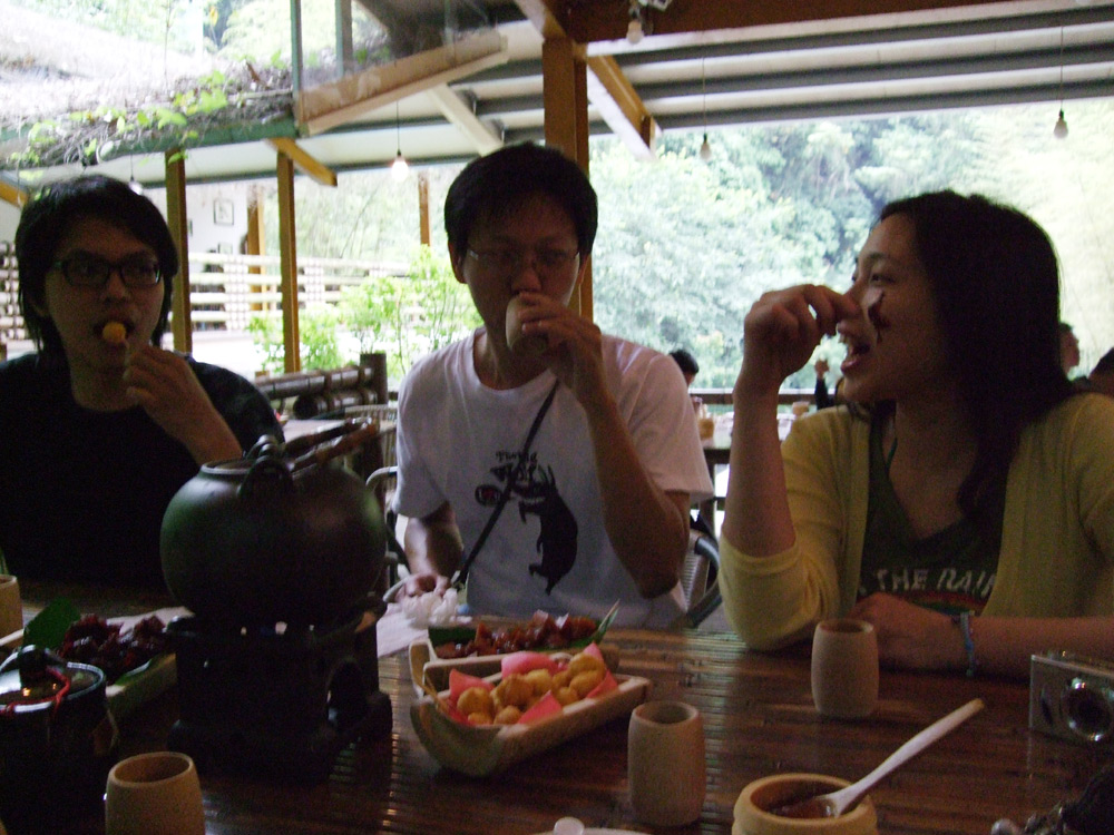 three young men eating food while talking on their cell phones