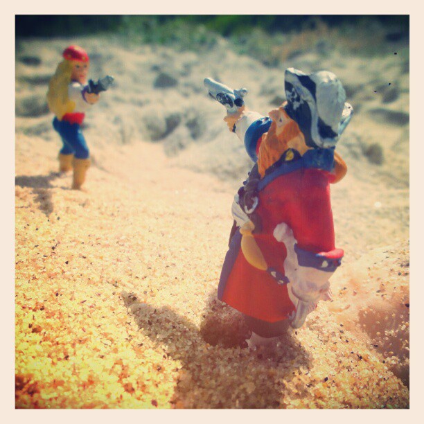 two action figures with toy guns and hats on a sandy surface