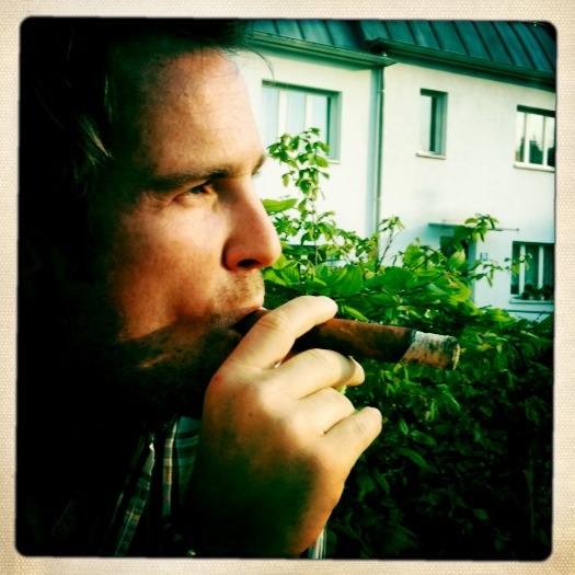 a man is biting his cigar with a house in the background