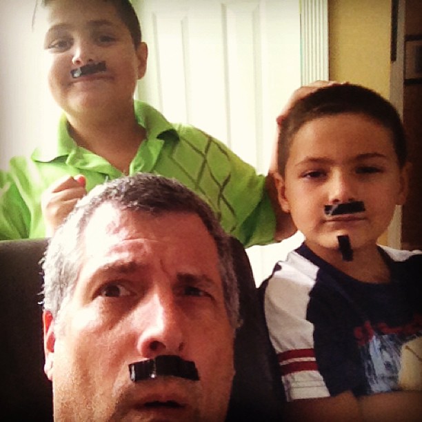 four boys sitting together with their mustaches on
