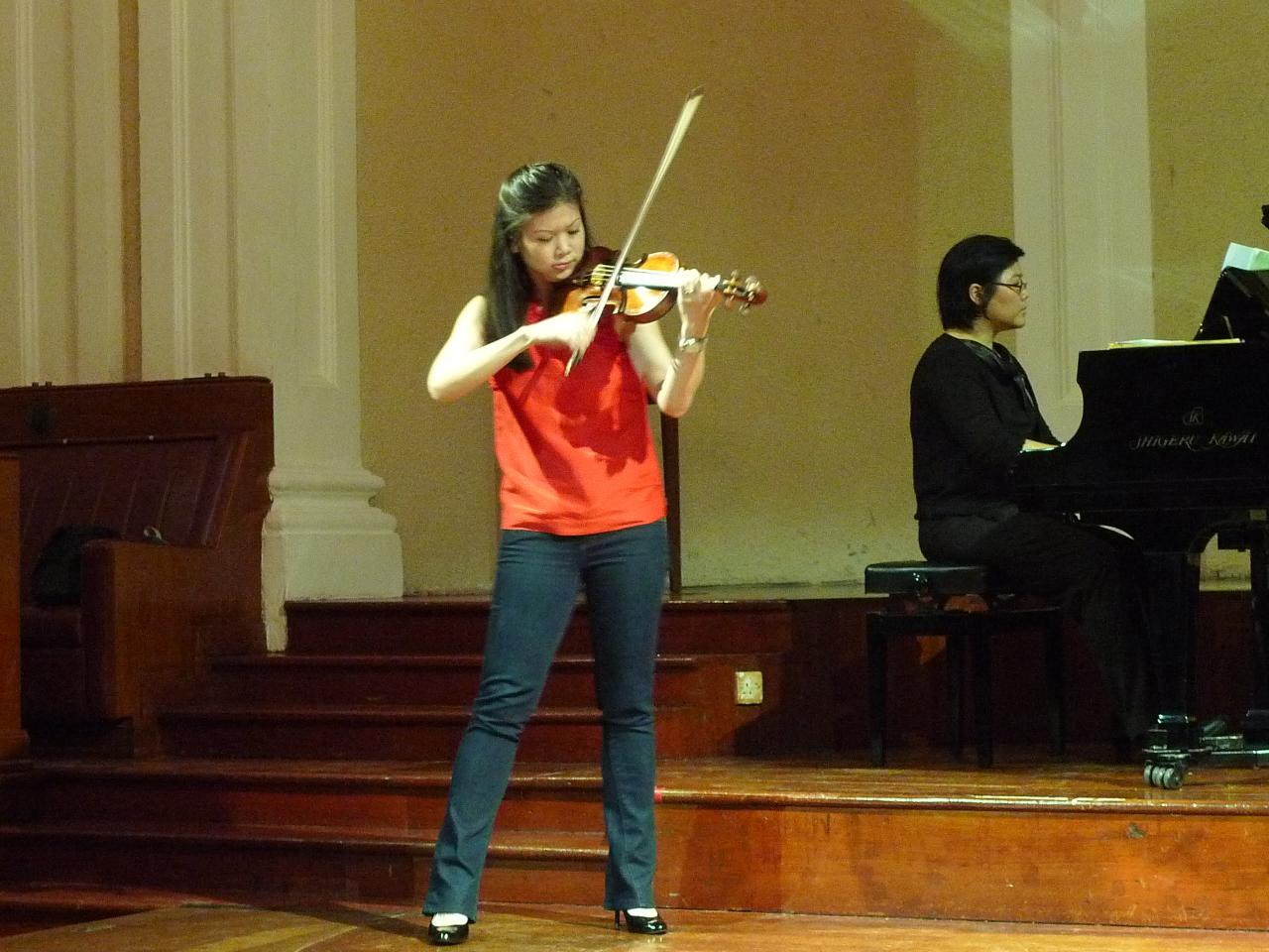 a woman is playing a violin in front of a piano