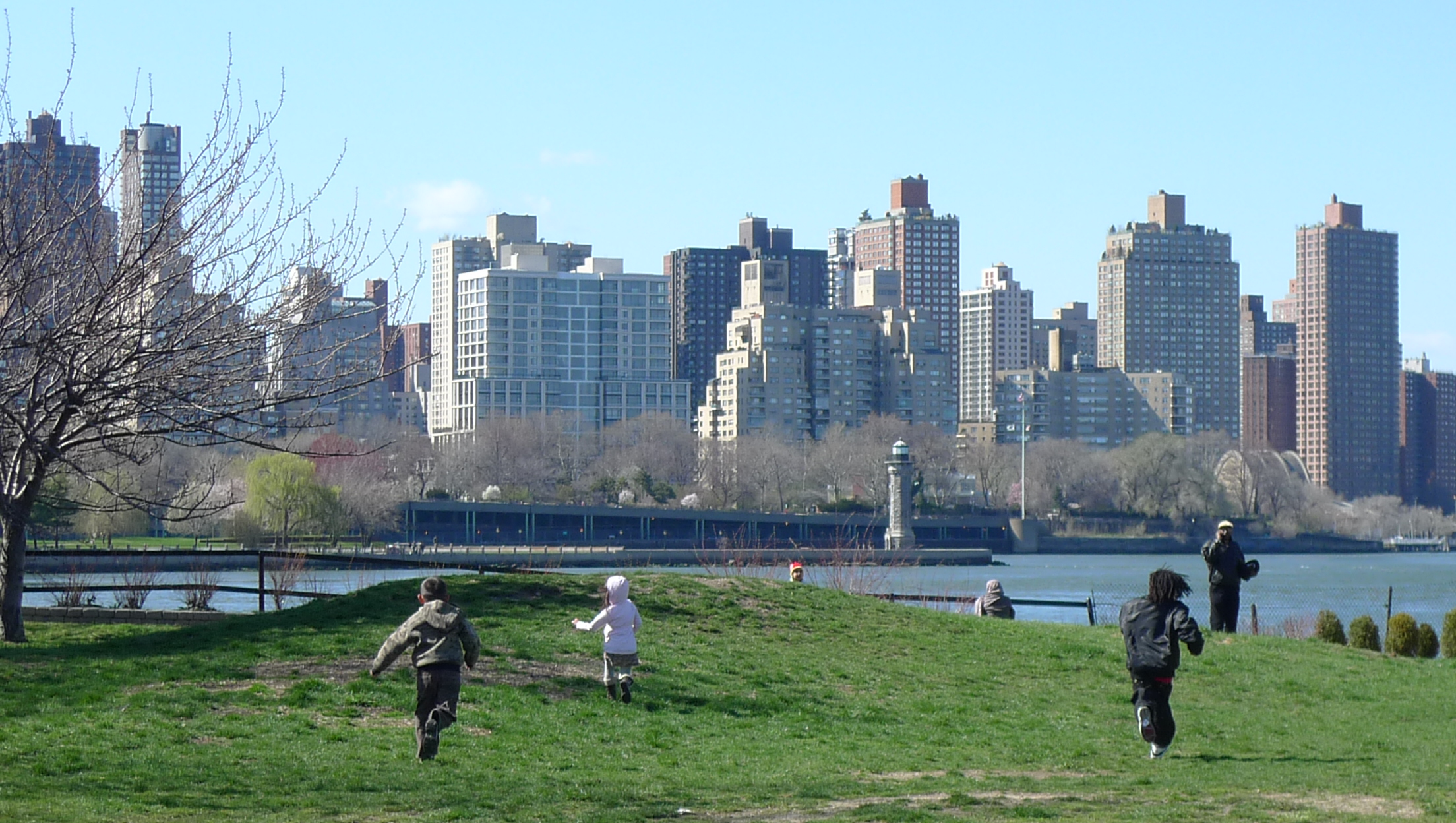 three children are running in the park by some water