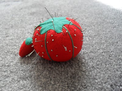 a small red strawberry on carpet with pins