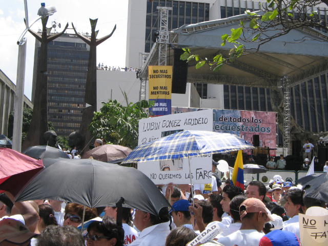 people gathered on the street in a city with large banners, umbrellas and signs