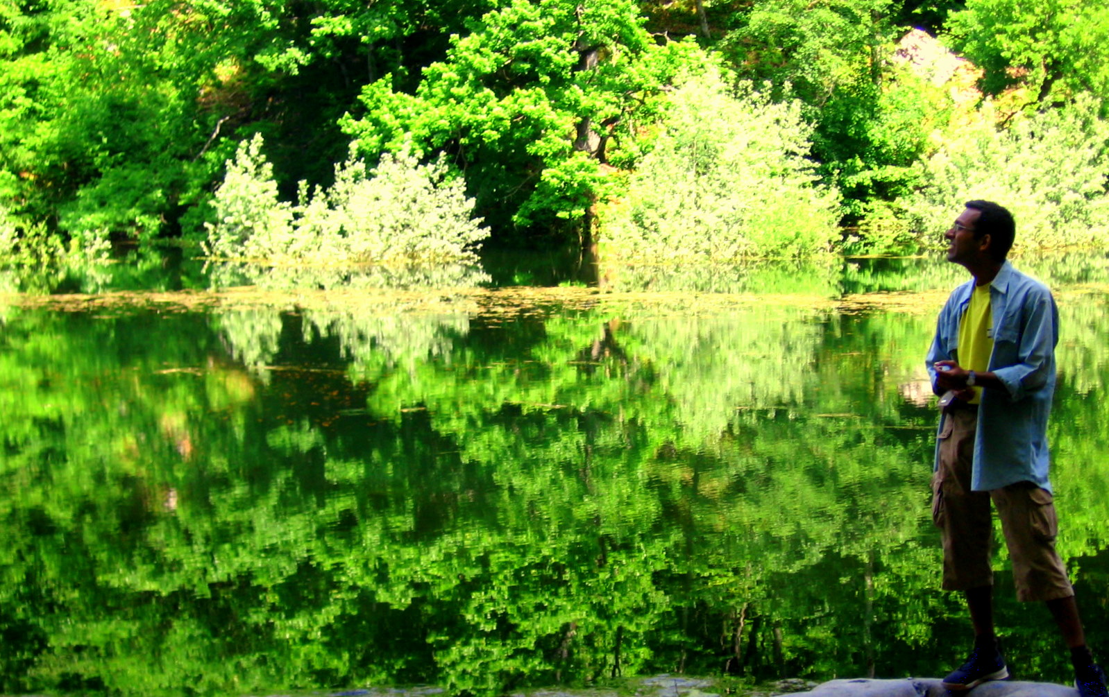 a man stands near the water with trees in the background