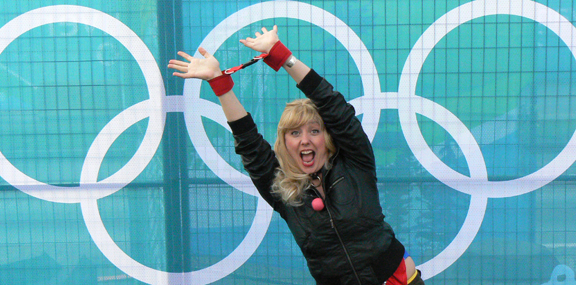 a woman posing for a picture in front of a wall that has a sign in it and olympic rings behind her