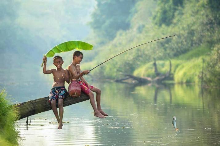two children on the side of a river hanging out on a log with a green leaf