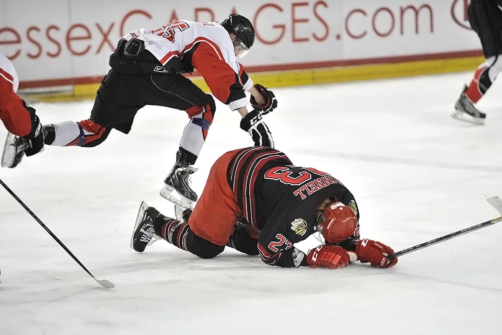 a hockey player falling on the ice to try and grab a goalie