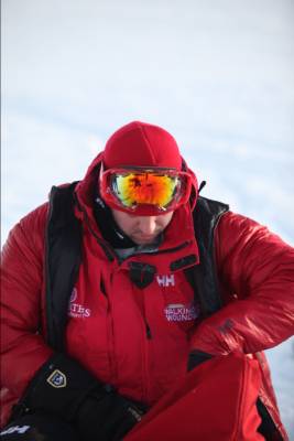 a man standing in snow with snowboard, sunglasses and red jacket