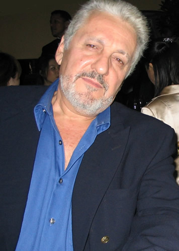 an older man in a blue shirt with a beard sits next to other people