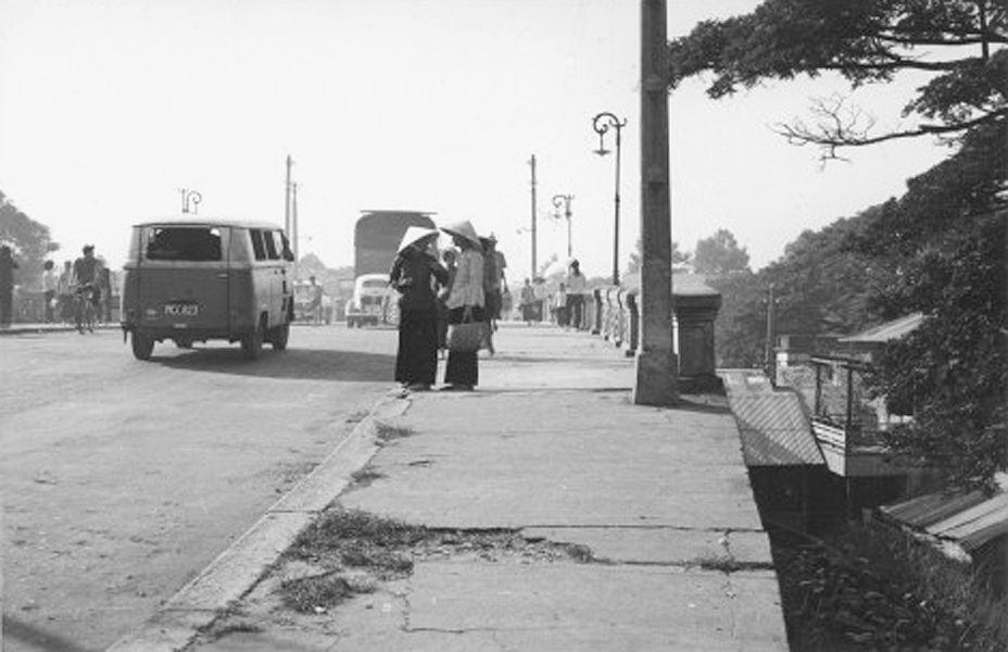 a black and white po shows two people standing at the curb of a busy street