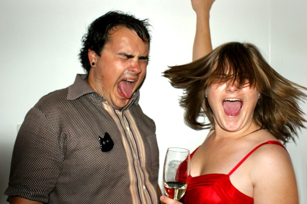 two people holding up glasses of wine and shouting