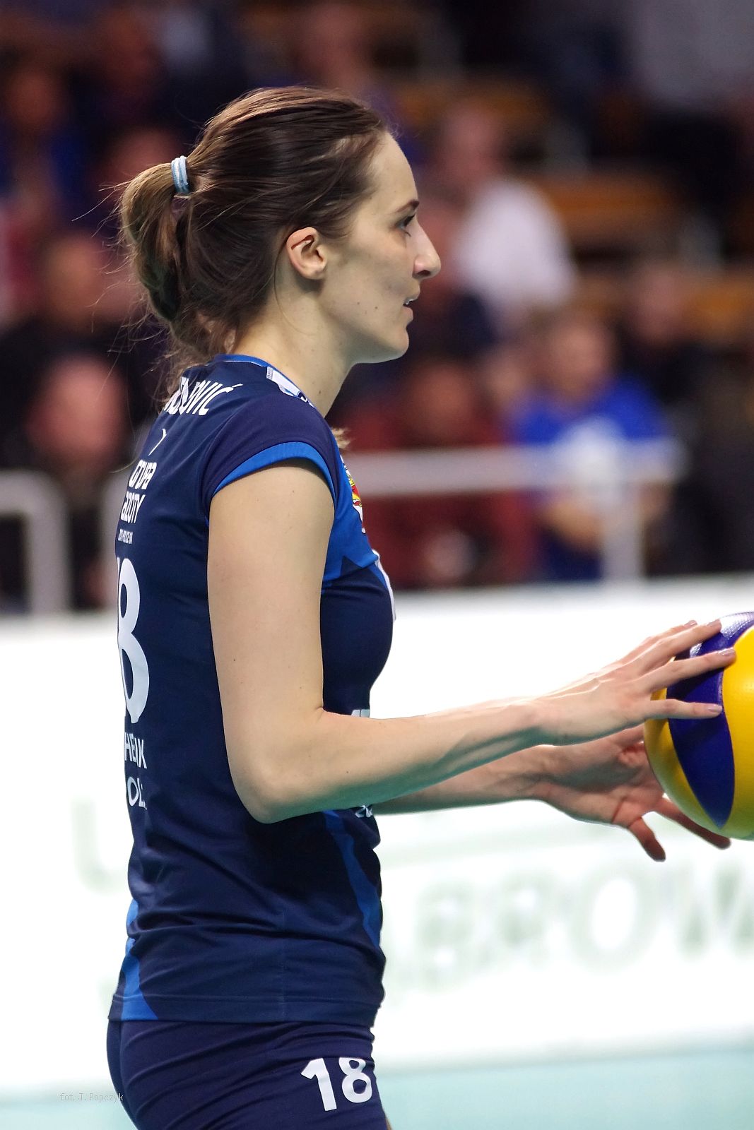a woman wearing a blue uniform holds a yellow and blue volleyball ball