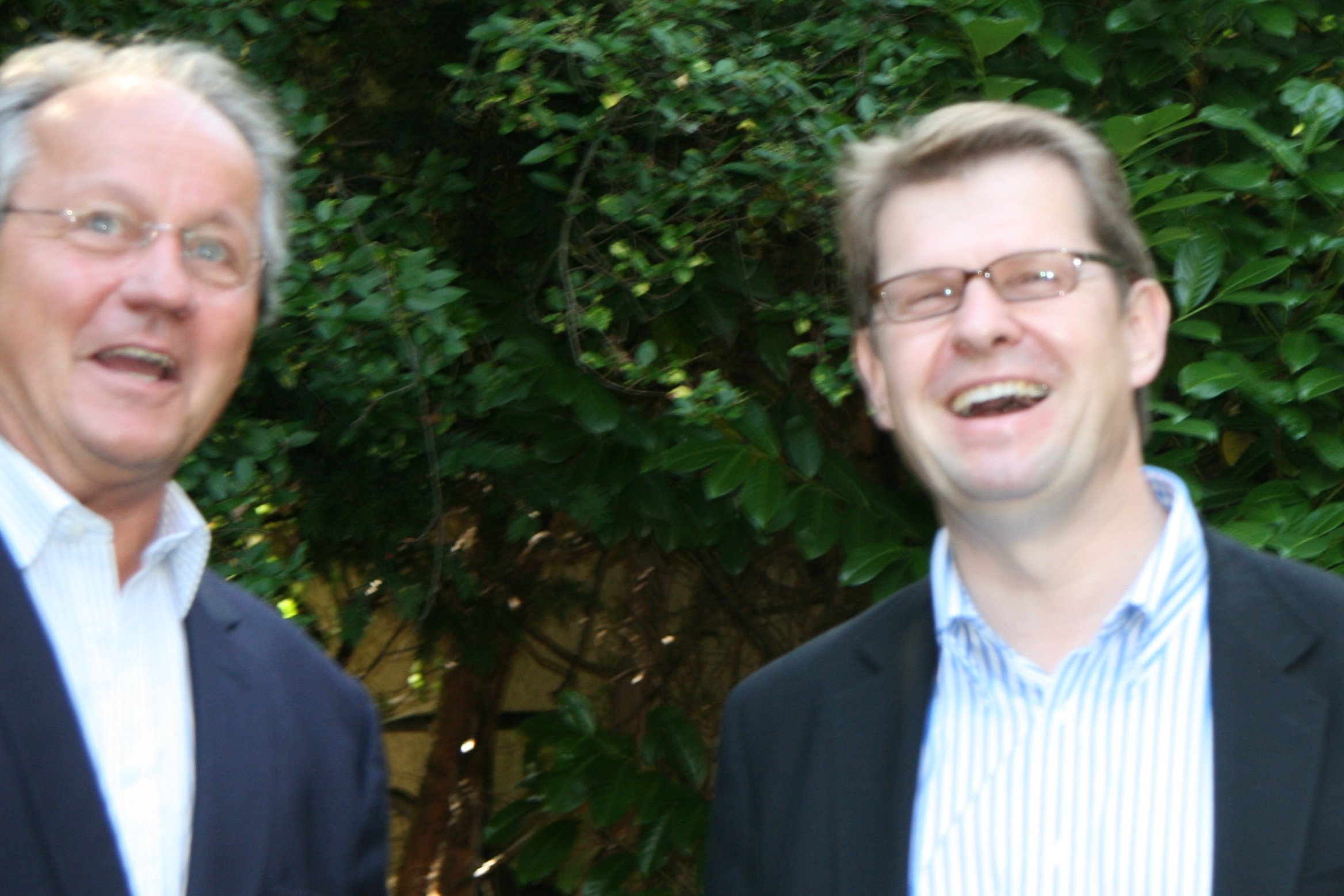 two older men standing near one another smiling