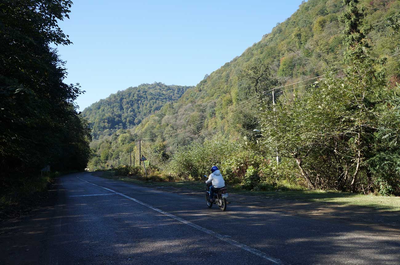 a person rides a motorcycle down the empty road in the mountains