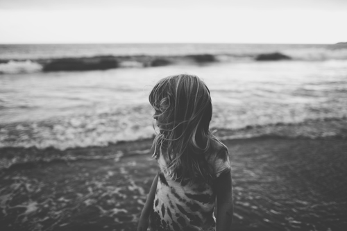 a girl is standing on a beach looking at the water