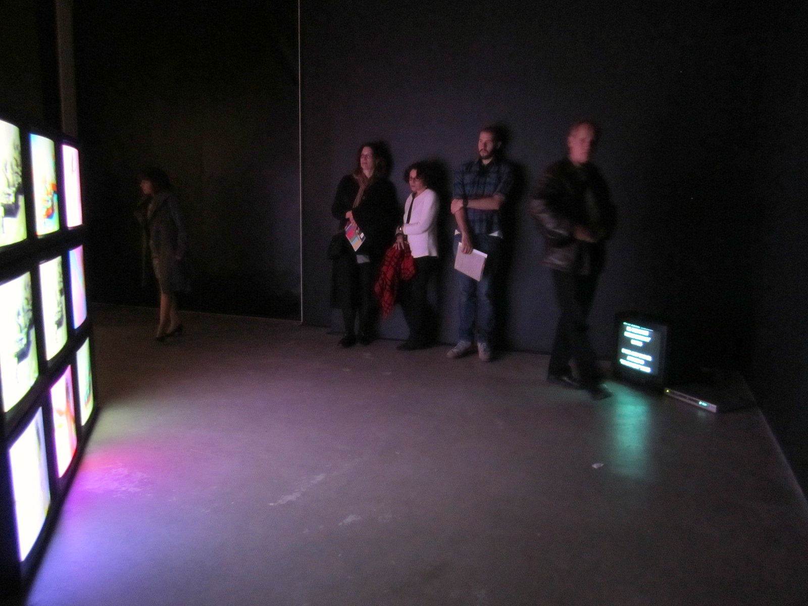group of people standing in dark room near four digital screens
