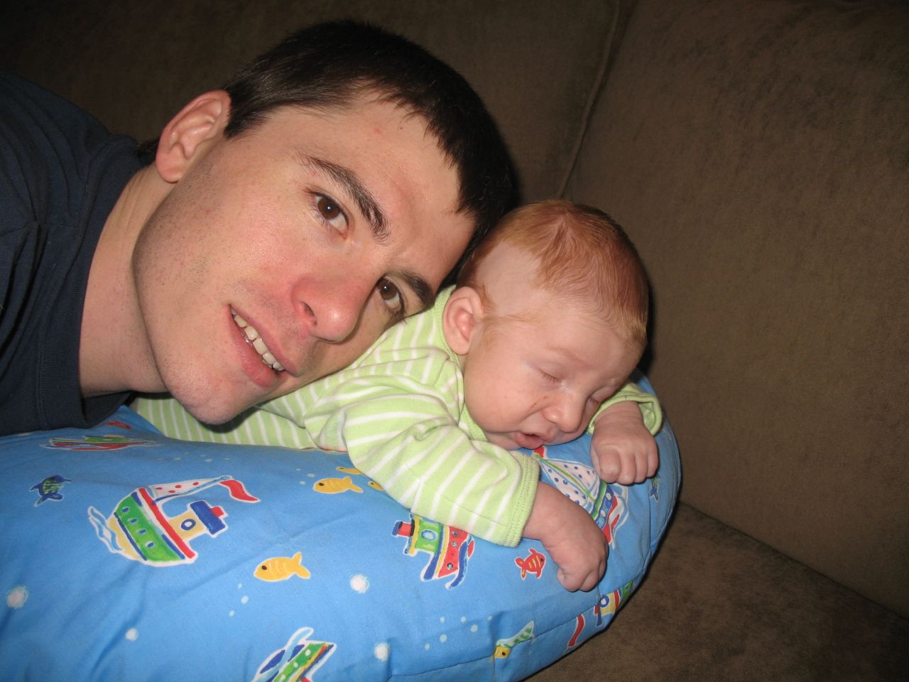 a man lying on a couch with a baby and smiling at the camera