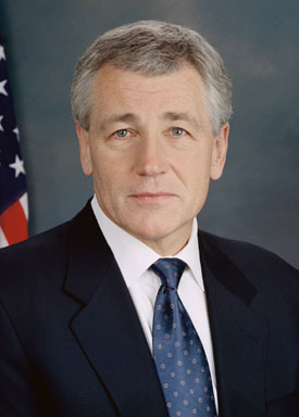a man in a suit and tie standing with an american flag behind him
