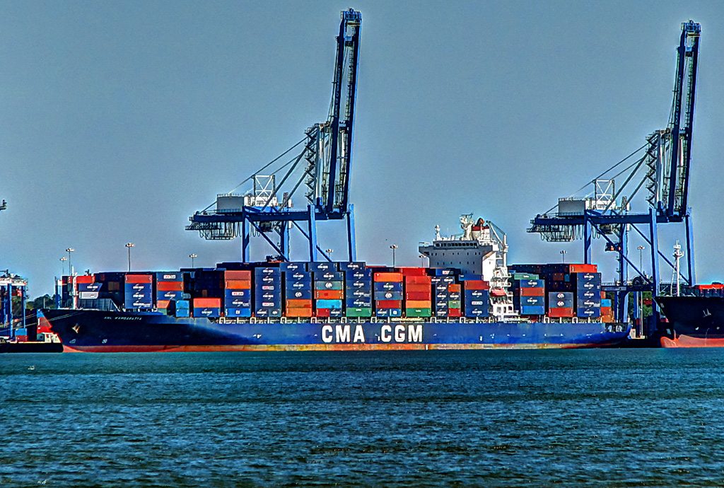 a large ship in the water with blue containers and cranes