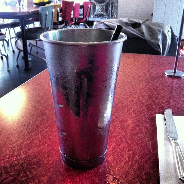 a glass is sitting on the table near a silver fork