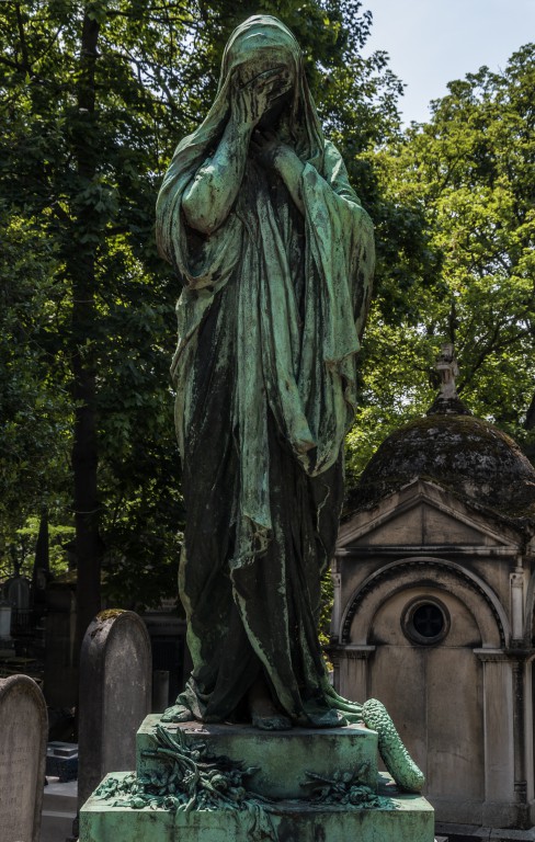 a statue stands in front of a gravestone with a cemetery in the background