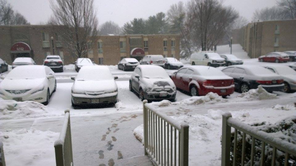 snow is piled up and parked cars outside buildings