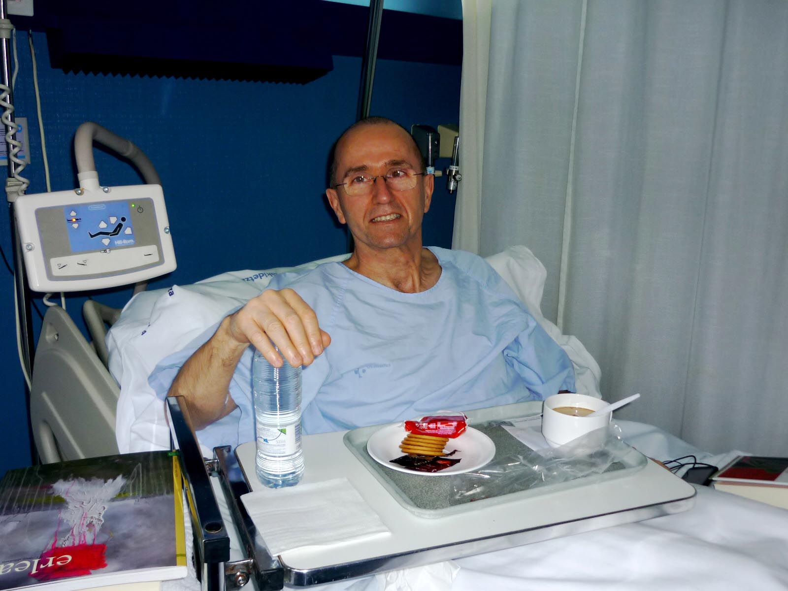 a man in a hospital room sitting in his bed holding a water bottle