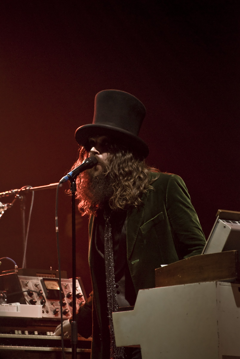 bearded man in a black top hat and suit playing an organ