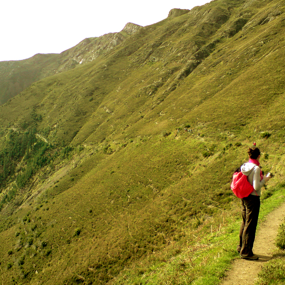 a man with a backpack walks along a path on the side of a hill
