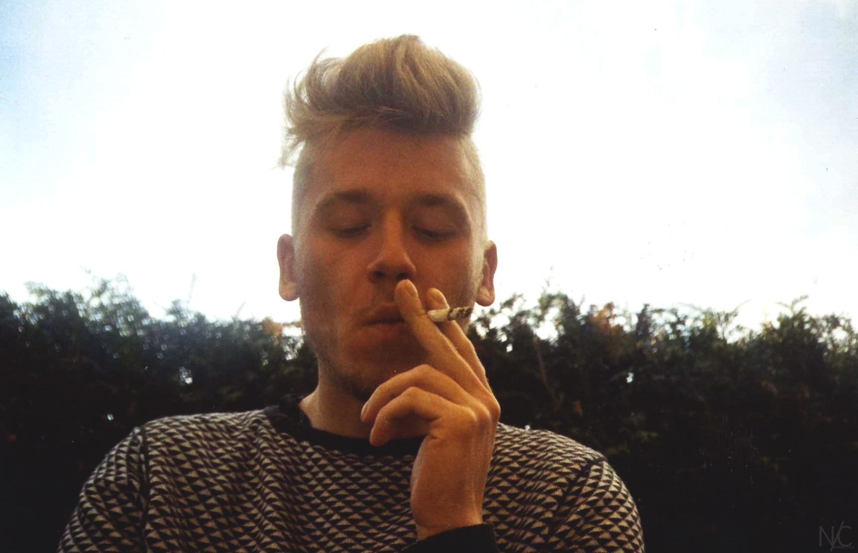 a man is smoking a cigarette outside by some bushes