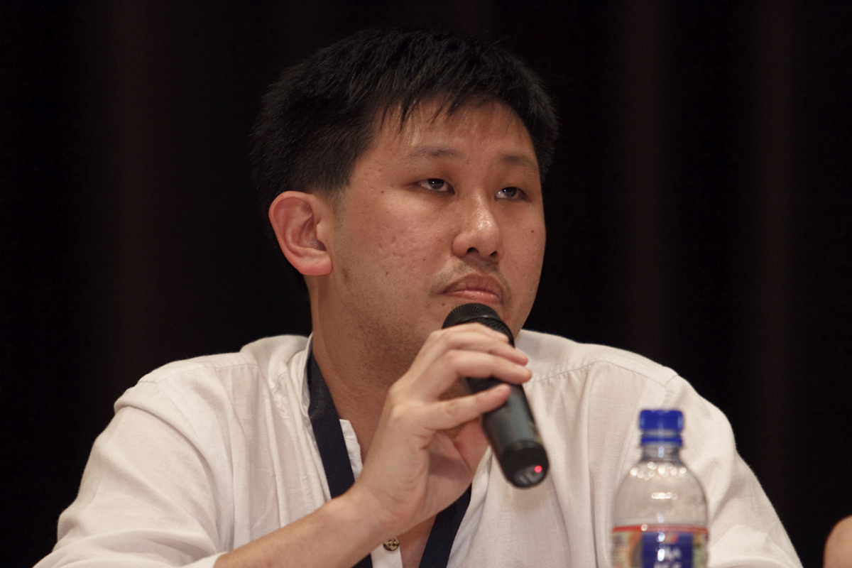 asian man holding microphone over right ear at a microphone