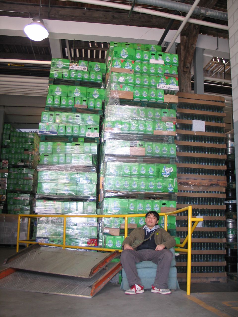 an asian man sits on a chair and a huge stack of bottles