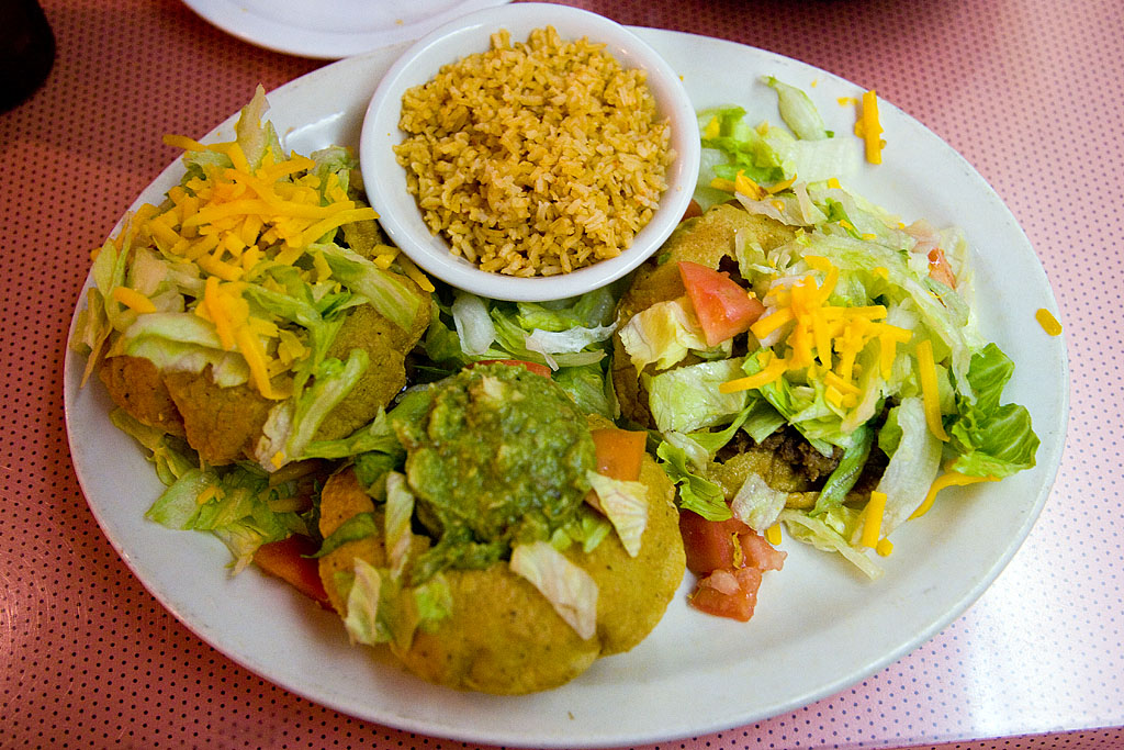 a plate full of tacos and rice topped with guacamole