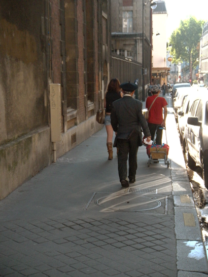 two people hing carts down the sidewalk with their backs against a building