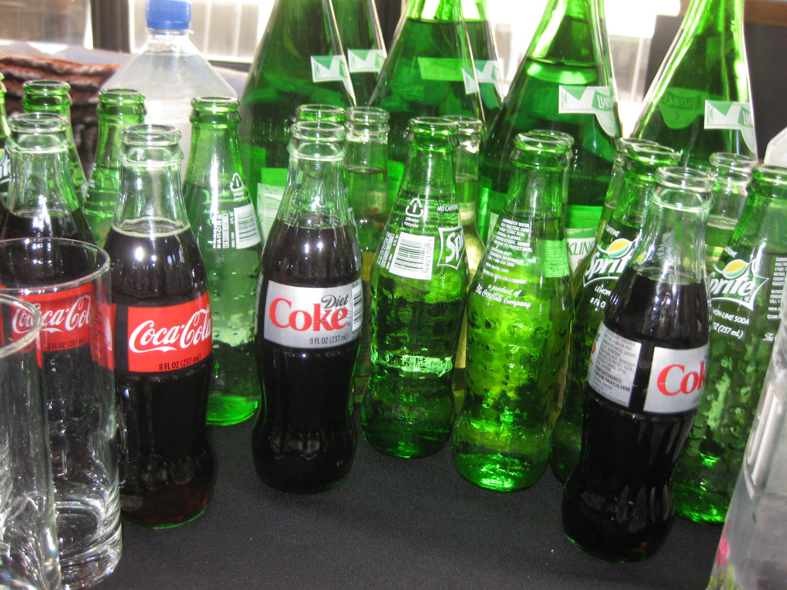 several rows of plastic coca - cola bottles displayed in glass on table